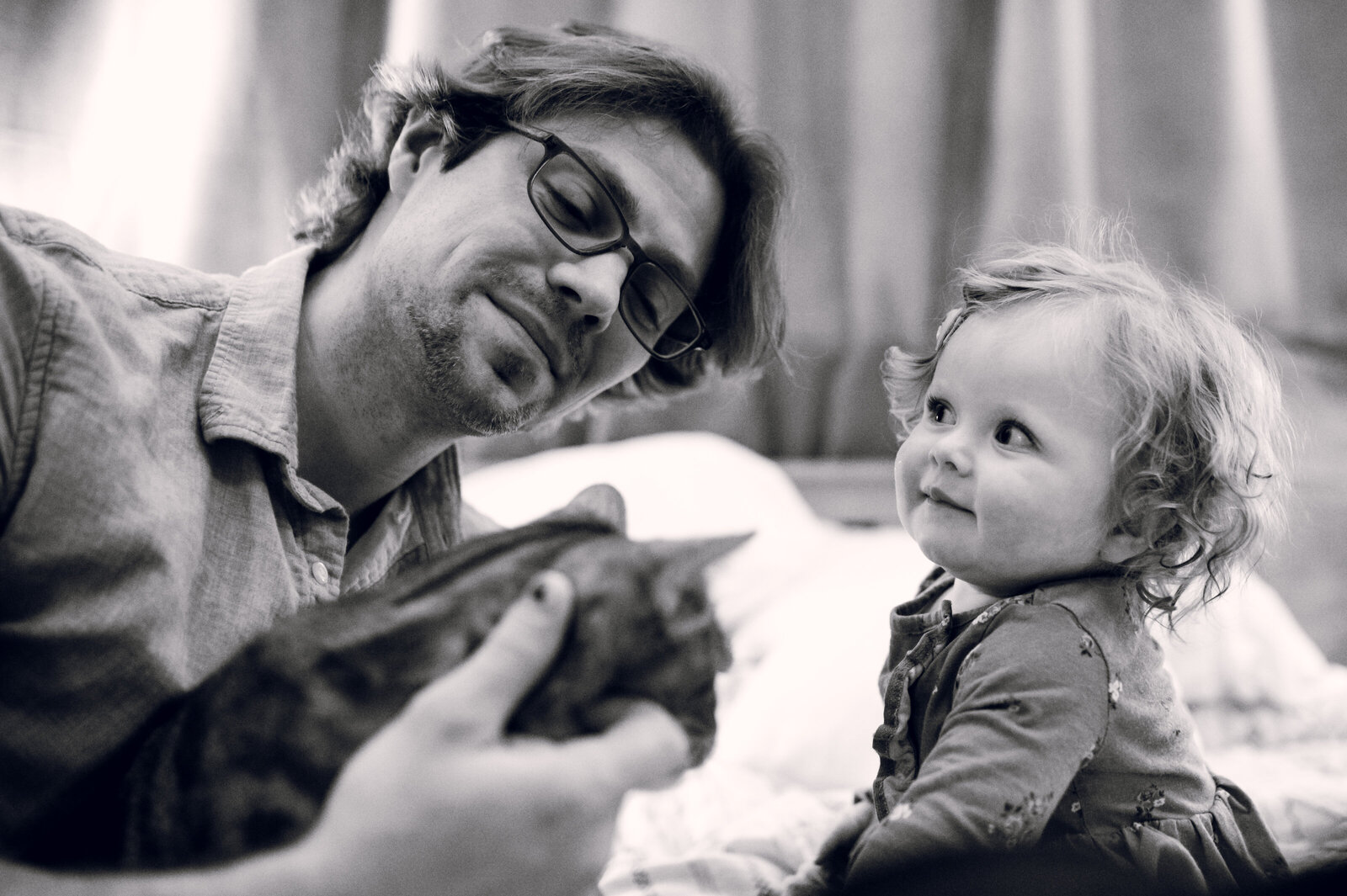 little girl looking at dad while he pets a cat