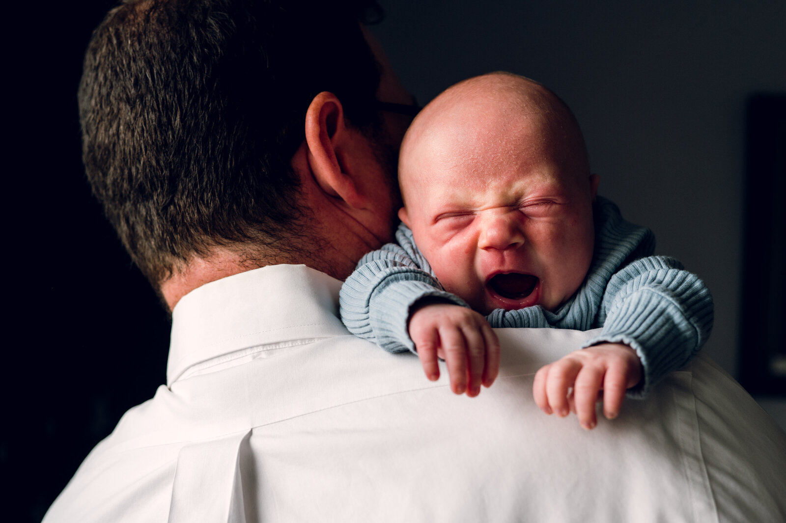 baby yawning while laying on a man's shoulder